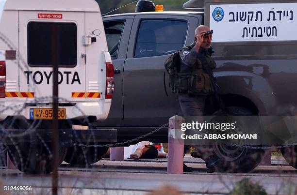 An Israeli security forces member walks next to the body of a Palestinian man who tried to stab Israeli soldiers before being shot dead at a...