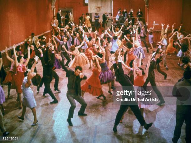 Young men and women dance with their arms thrust into the air inside a gymnasium during a musical number from the film, 'West Side Story,' directed...