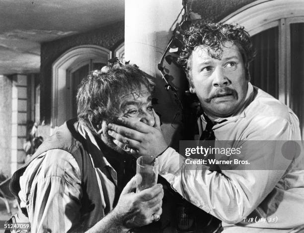 British actor Peter Ustinov, right holds his hand over the mouth of Russian actor Akim Tamiroff in a still from the film, 'Topkapi' directed by Jules...