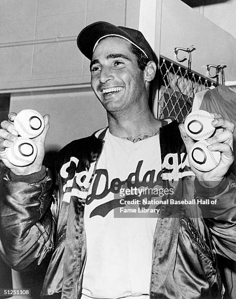 Sandy Koufax of the Los Angeles Dodgers holds four baseballs with zeroes on them to signify his 4th no-hitter which was also a perfect game, against...