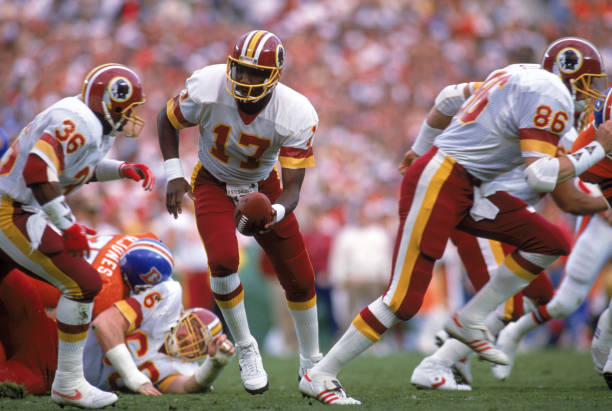 Quarterback Doug Williams of the Washington Redskins prepares to hand of the ball to running back Timmy Smith during Super Bowl XXII against the...