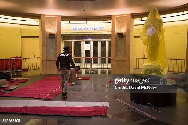 Workers cut and measure red carpet next to an Oscar statue wrapped in yellow plastic at the entrance to the Dolby Theatre as preparations continue...