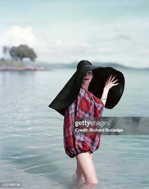 Model wearing enormous floppy straw hat in navy blue, with purple, red and black cape, on the US Virgin Islands.