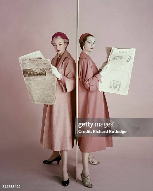 Two models reading newspapers wearing similar coats by Gaynes: a coat with slope-shoulders and a straight-and-narrow shape made in a washable cotton...
