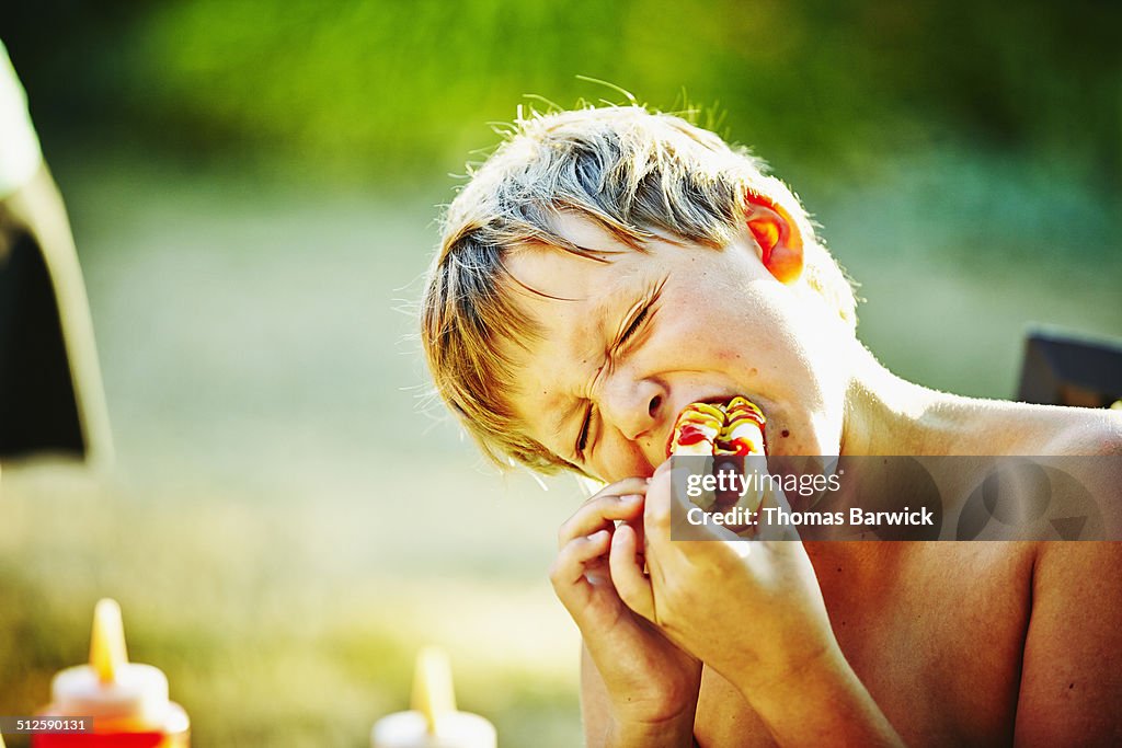 Young boy taking bite of hot dog at barbecue