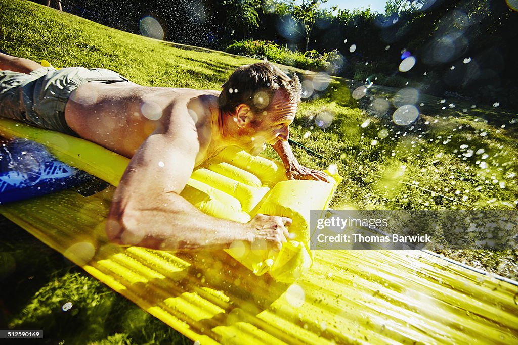 Smiling father on water slide in backyard