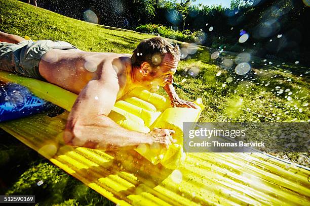 smiling father on water slide in backyard - tobogán de agua fotografías e imágenes de stock
