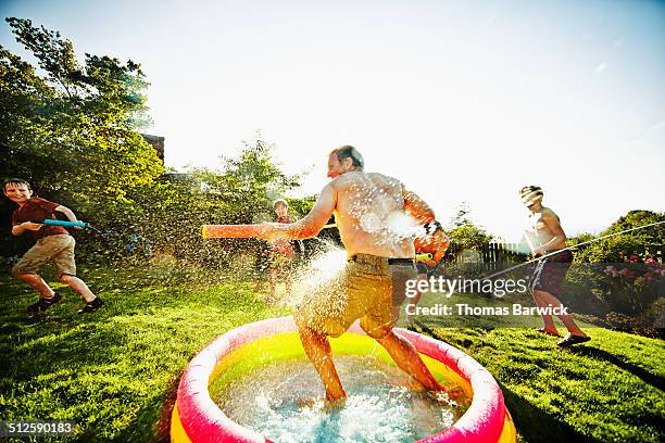 laughing dad in water fight with kids in backyard - waterpistool stockfoto's en -beelden