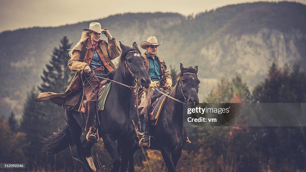 Cowboy and cowgirl riding on horses through the woods