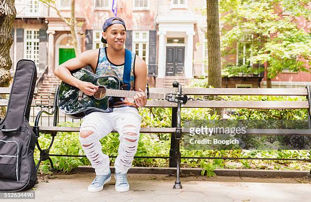 smiling young black man playing acoustic guitar in nyc park - washington square park stockfoto's en -beelden