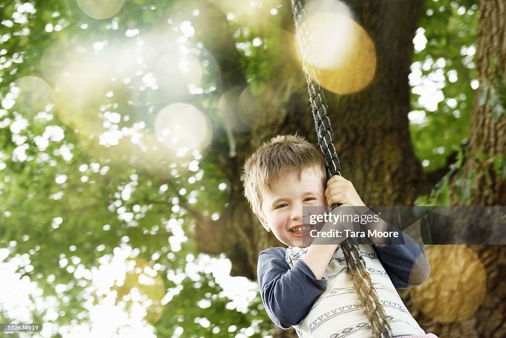 Young boy swinging on rope in park