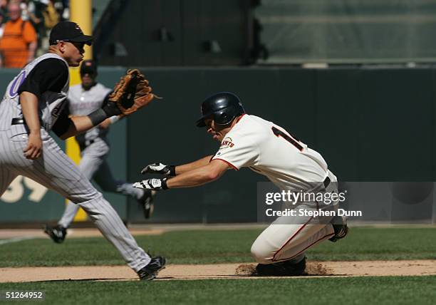 Brian Dallimore of the San Francisco Giants slides safely into third base after a two base throwing error as shortstop Alex Cintron of the Arizona...