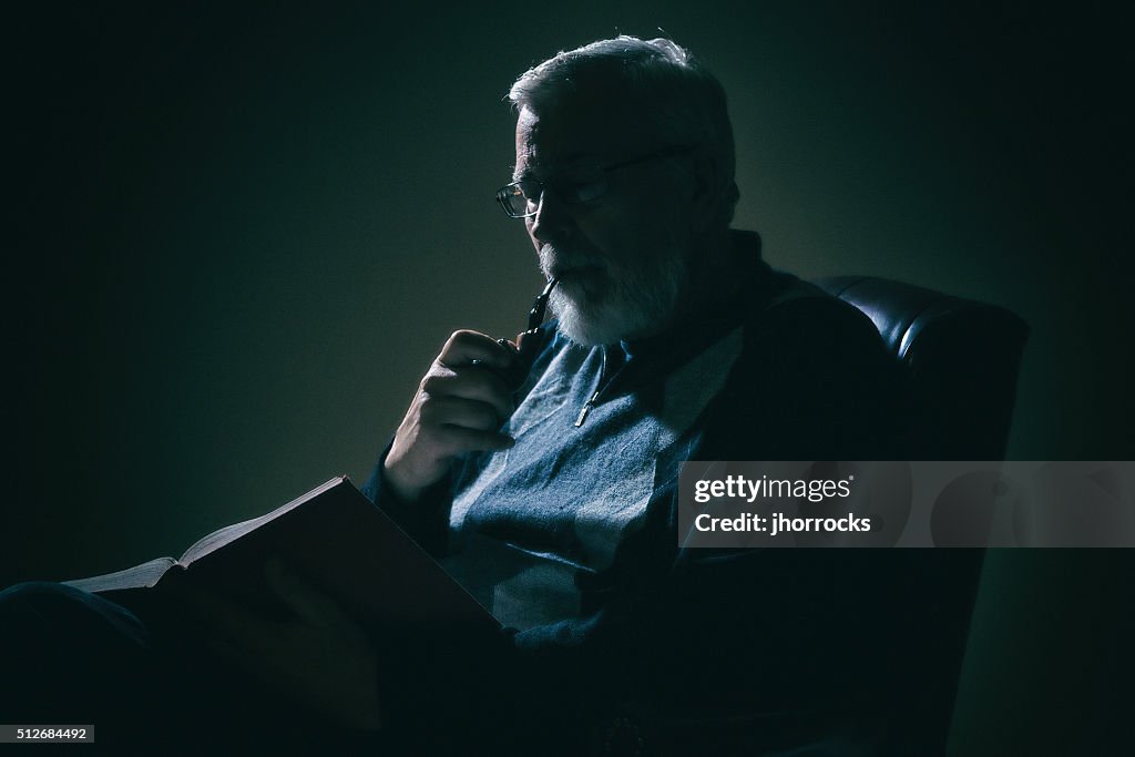 Senior Man Reading a Book in Dimly Lit Room