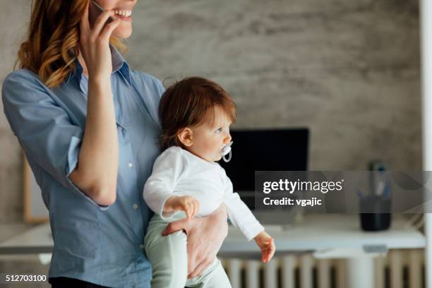 mutter reden am telefon und hält ihr baby - leanincollection working mom stock-fotos und bilder