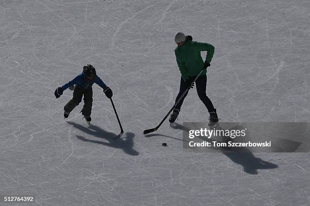 Mother and her son practice on an ice pad adjacent to outdoor shinny hockey action during the 7th Annual Lake Louise Pond Hockey Classic on the...