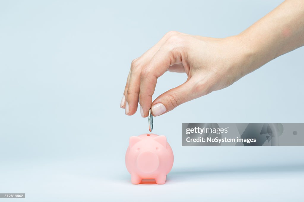 Female hand putting a coin into piggy bank