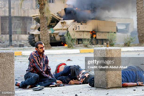 Dead and critically injured Iraqi civilians are seen lying in the street as a US military vehicle burns in the background on September 12, 2004 in...