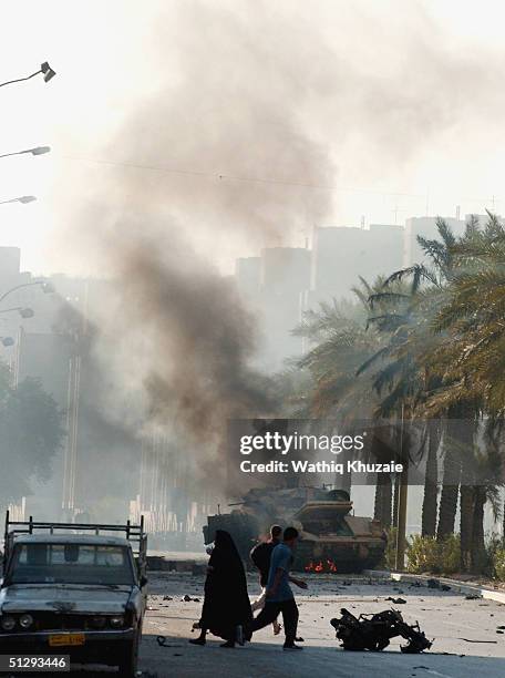 Iraqis cross the street as a US military vehicle burns in the background on September 12, 2004 in Haifa Street, Baghdad, Iraq. Fighting broke out in...