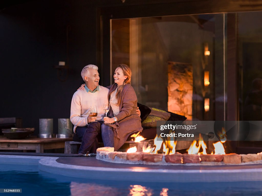 Couple sitting at poolside by fire pit at night