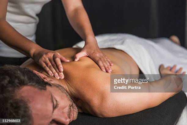man receives back massage in spa - massage table imagens e fotografias de stock