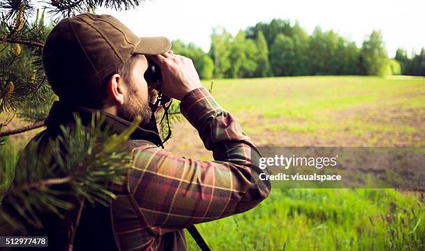 hunter looking over the field through binoculars - jager stockfoto's en -beelden