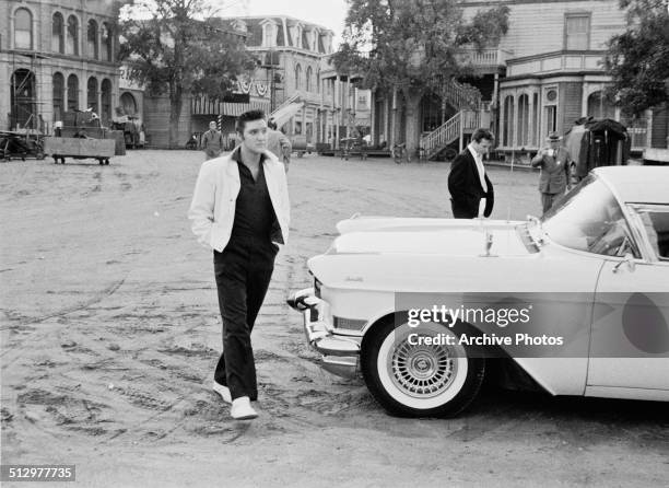 American rock n' roll singer and actor Elvis Presley walking past a Cadillac Eldorado on a movie set, USA, circa 1958.