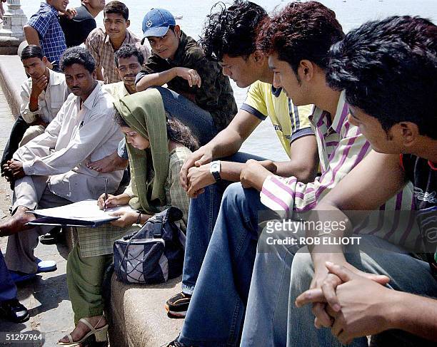 Indian men sit around and watch a female arts student as she sketches in Bombay, 13 September 2004, near the departure point for ferries going to...
