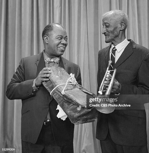 In a scene from the television game show 'I've Got a Secret,' American jazz musician Louis Armstrong holds a battered trumpet case as he is reunited...