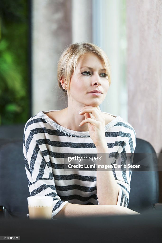 Mid adult woman in striped shirt sits in cafe musing