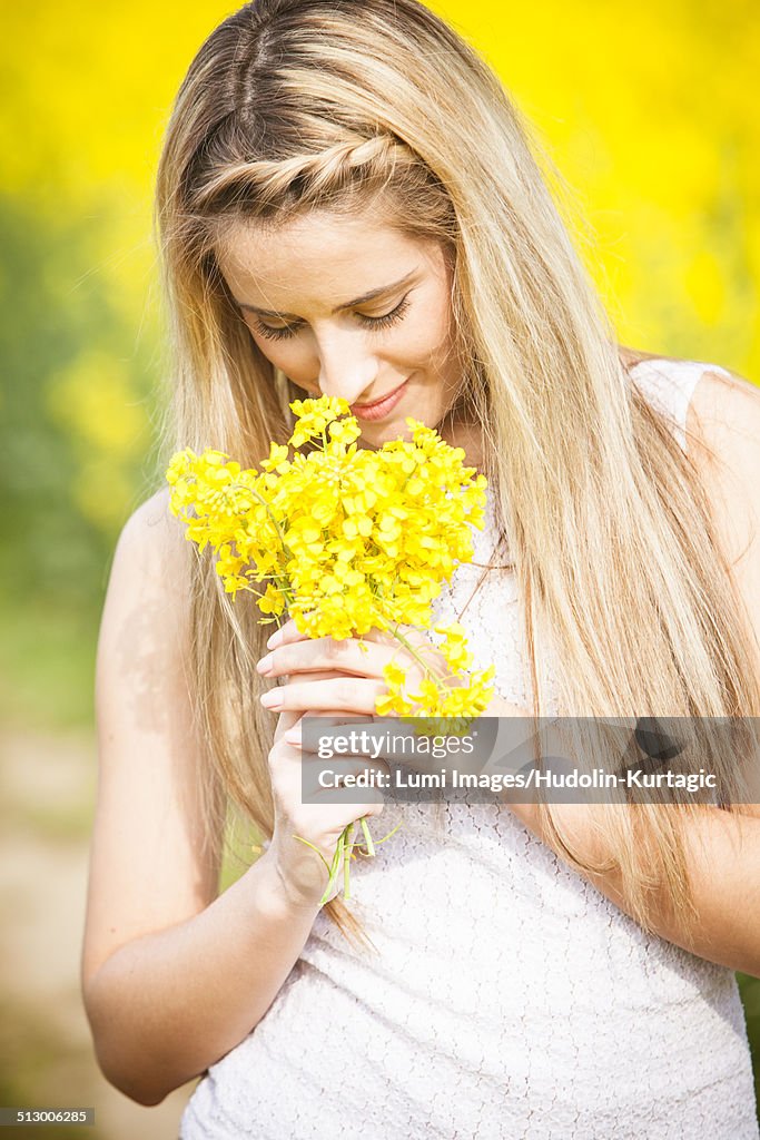 Young woman smelling colza flowers, Tuscany, Italy