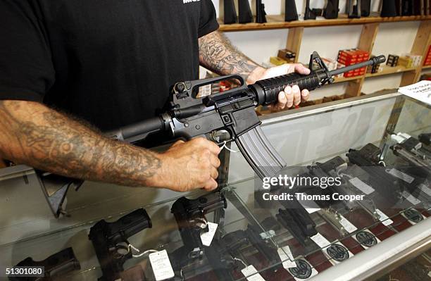 An employee of Dave's Guns holds a Colt AR-15, now legal with a bayonet mount, flash suppressor, collapsible stock and a high capacity magazine that...