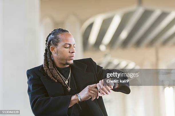 young mixed race man in black coat looking at watch - rapper chain stock pictures, royalty-free photos & images