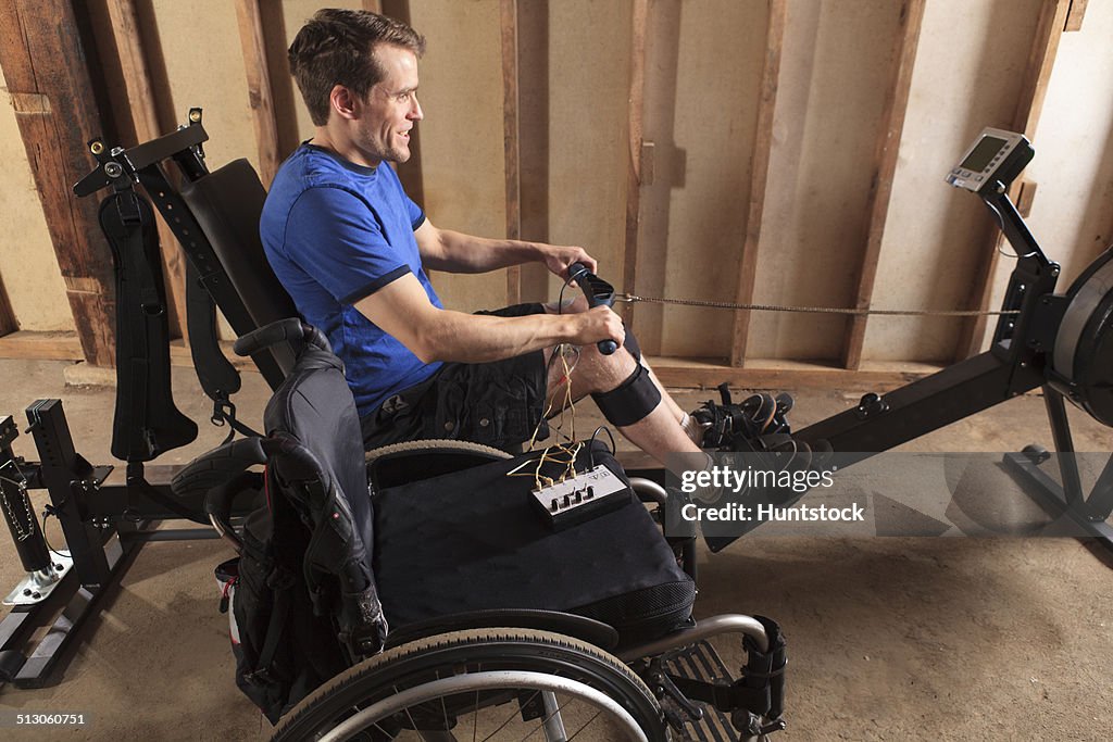 Man with spinal cord injury using his rowing machine with a muscle stimulator attached