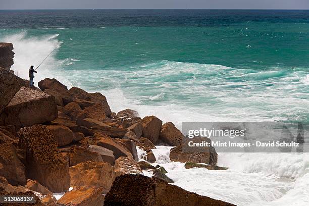 a fisherman standing on the rocks surf casting in the white waves on the atlantic coast. - surf casting stock pictures, royalty-free photos & images