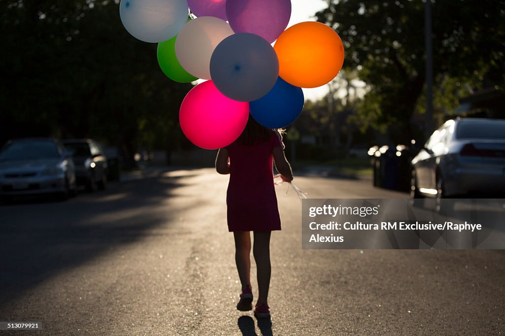 Rear view silhouetted shot of girl walking along road with bunch of balloons