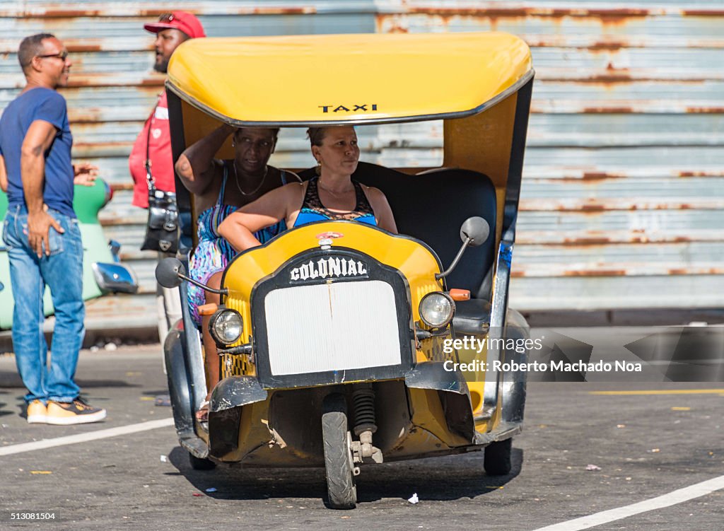 Woman driving three-wheeled yellow Coco taxi. Coco-taxi are...