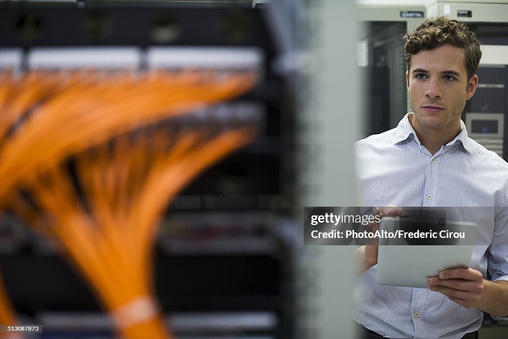 Computer technician using digital tablet performing maintenance check of mainframe equipment
