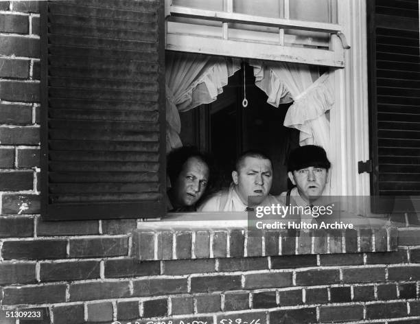 The Three Stooges peer out of a window in a still from an unidentified film. L-R: American actors Larry Fine , Curly Howard , and Moe Howard .