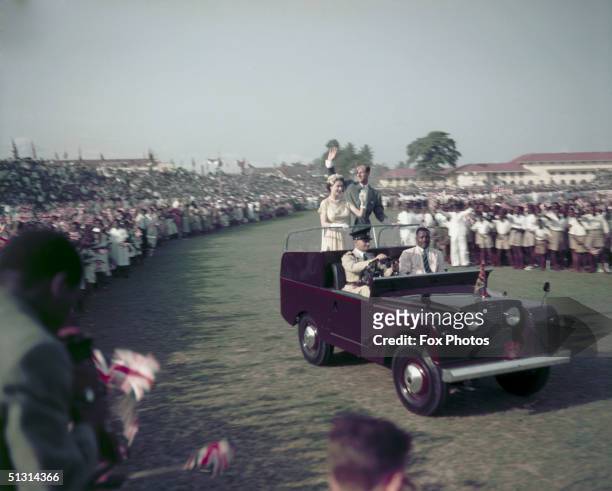 Queen Elizabeth II and Prince Philip waving from a Land Rover at a youth rally on the racecourse at Lagos, Nigeria, 10th February 1956.