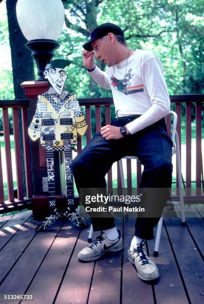 Portrait of American musician Rick Nielsen, of the band Cheap Trick, as he poses with one of his guitars on the porch of his home, Rockford,...
