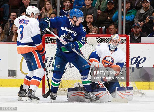 Travis Hamonic of the New York Islanders and Bo Horvat of the Vancouver Canucks watch Thomas Greiss of the Islanders make a save during their NHL...