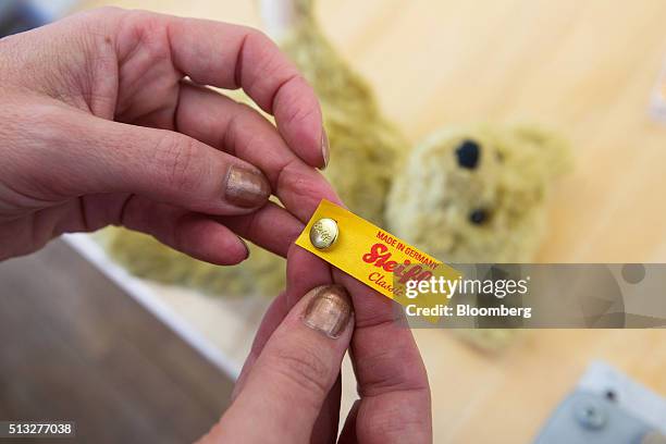 An employee holds an ear button and logo label marked "Made in Germany" during teddy bear manufacture inside the Steiff GmbH stuffed toy factory in...