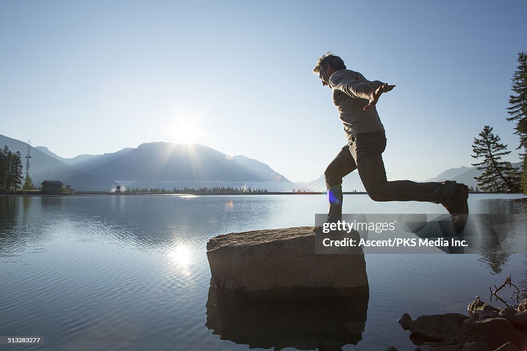 Man hops onto rock island, mountain lake
