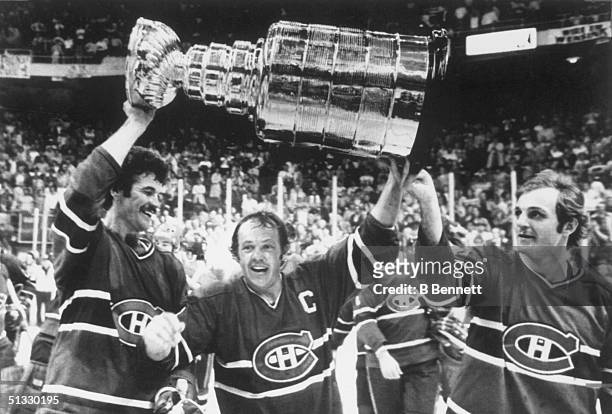 Yvan Cournoyer of the Montreal Canadiens, hoist the Stanley Cup Trophy with help from teammates Yvon Lambert and Guy Lafleur after defeating the...