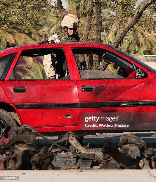 Soldier looks at a damaged civilian car at the scene of a car bomb explosion September 21, 2004 in Baghdad, Iraq. A car bomb exploded near a U.S....