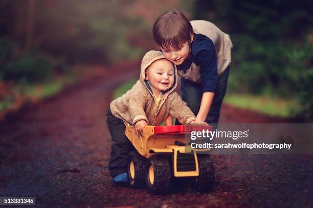 little boy and a baby pushing a dump truck together - baby sibling stock pictures, royalty-free photos & images