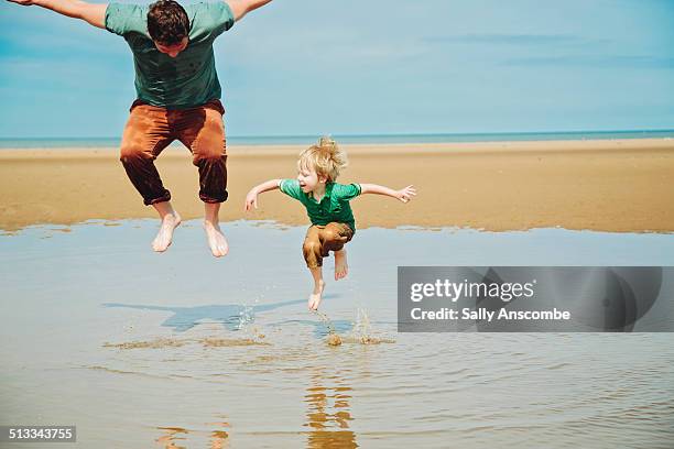 father and son playing on the beach together - jump dad stockfoto's en -beelden