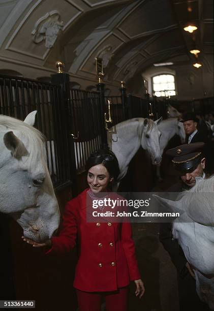 World Championships: Portrait of USA Peggy Fleming casual, posing with Lipizzaners horses in the stables of Spanish Riding School. Vienna, Austria...