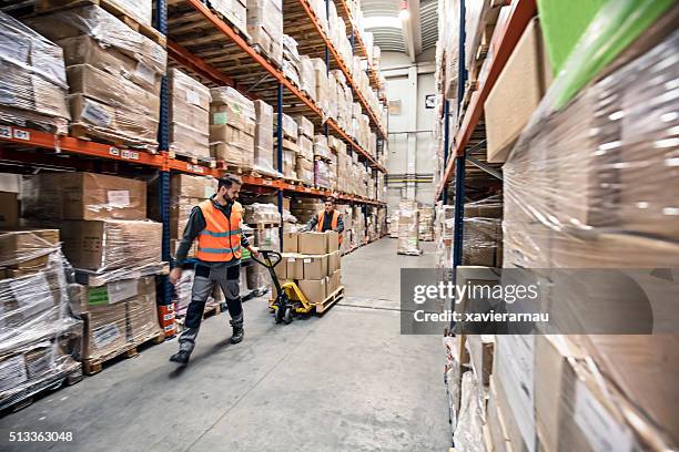 workers transporting boxes in warehouse - pallet stockfoto's en -beelden