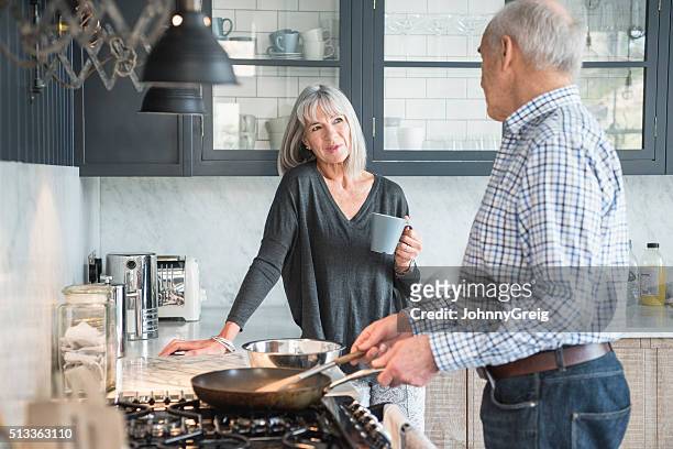 senior couple in a kitchen making dinner and talking - 60 woman stockfoto's en -beelden